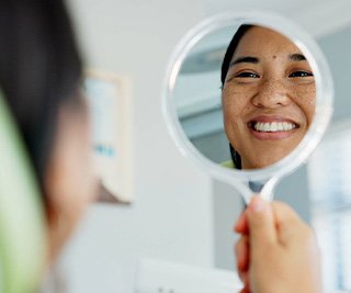 Woman smiling at reflection in handheld mirror