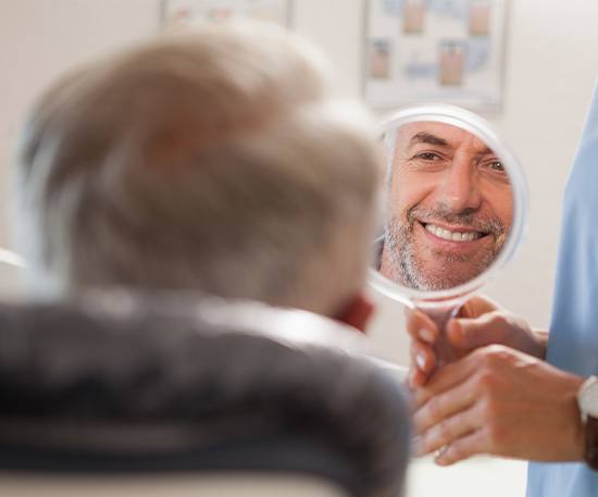 Older man in dental chair looking at his smile