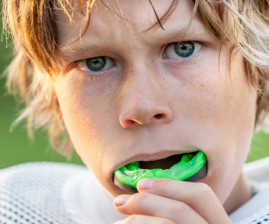 Teen boy placing green athletic mouthguard