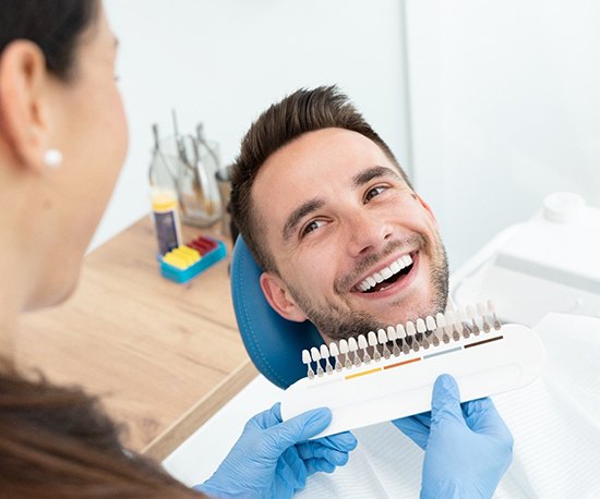 A dentist using a shade guide to determine the color of a male patient’s dental crown 