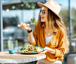 Woman sitting outside, eating a big, healthy salad