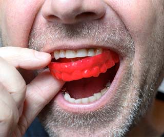 Close-up of man placing red mouthguard in his mouth