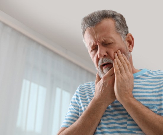 Man in striped shirt rubbing jaw due to pain