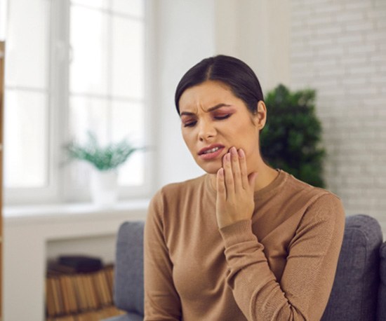 Concerned woman in a light brown shirt with pain in her jaw