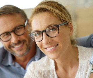 Couple who wears glasses smiling with arms around each other