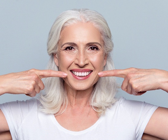 woman pointing to her smile with implant dentures in Murphy, TX