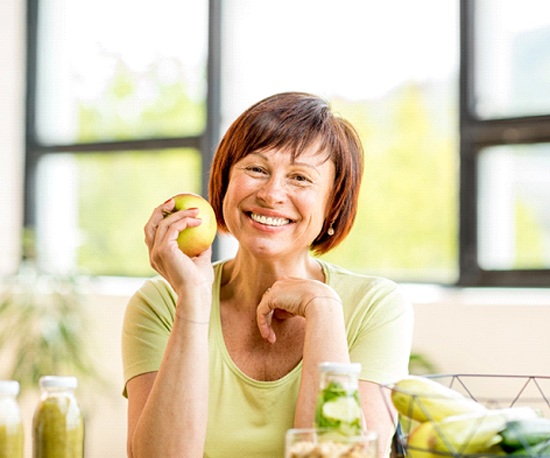 smiling woman sitting at her kitchen table and holding an apple