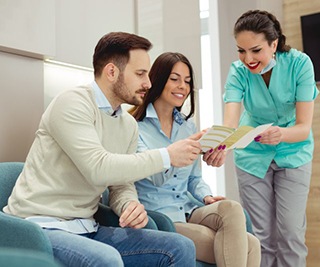 dental team member explaining the cost of dental implants to two patients 