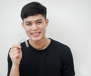 smiling young man holding a clear aligner