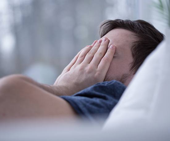 Frustrated man in bed covering his face