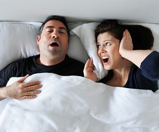 Woman covering ears next to snoring man