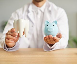 Dentist holding a large tooth in one hand and blue piggy bank in the other