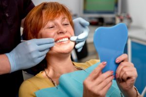 a woman smiling at her dental implants in the mirror