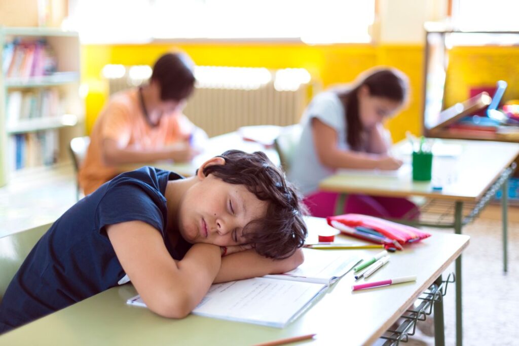 A little boy asleep at his desk at school