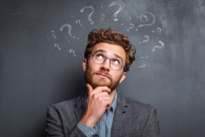 Curious man standing in front of chalkboard with question marks on it 