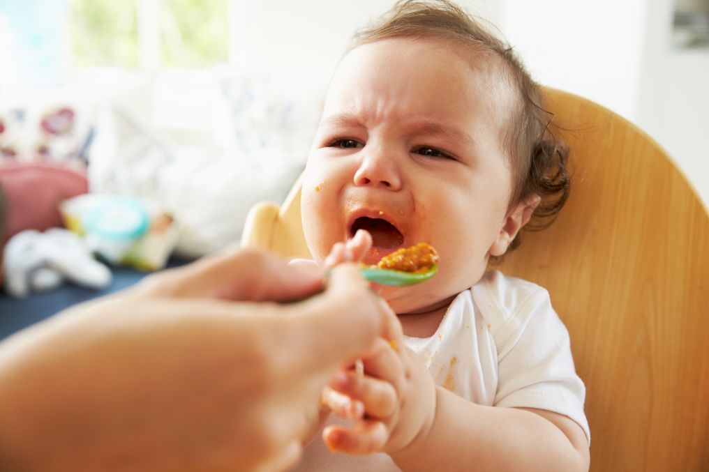A baby crying while being fed solid food