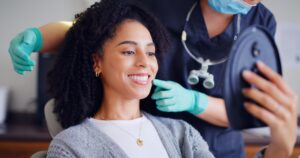 Woman in dental chair smiling into mirror with dentist touching her face with gloved hand